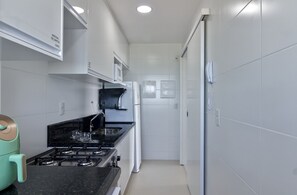A narrow kitchen with a gas stove, a microwave, and a refrigerator. - Palmer | Jockey de Itaparica | Panoramic View (Vila Velha)