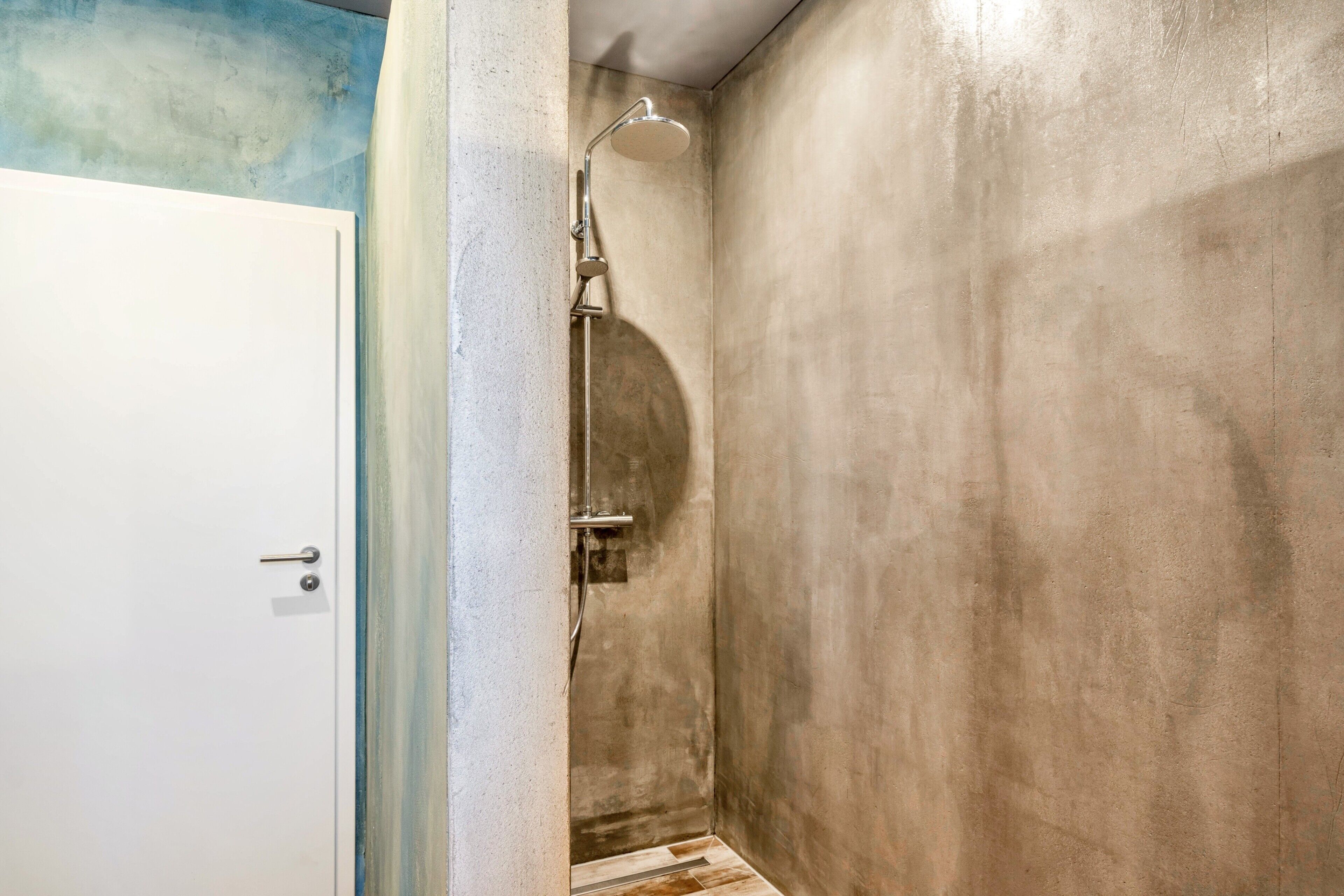 A bathroom with a shower, a white door, and a textured wall.