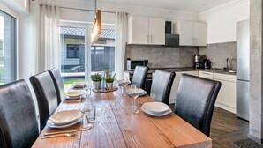 Una cocina moderna con armarios blancos, un refrigerador de acero inoxidable y un comedor con una mesa de madera dispuesta para seis comensales.