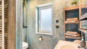 A bathroom with a toilet, a sink, a towel rack, a window, and a shelf with towels.
