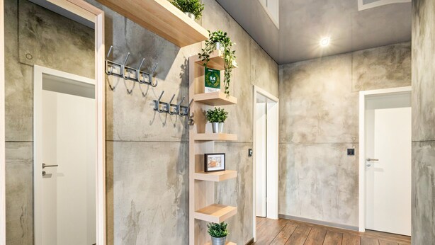 Un pasillo con pared de concreto, suelo de madera y estante empotrado con plantas y un cuadro enmarcado.