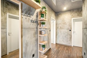Un pasillo con pared de concreto, suelo de madera y estante empotrado con plantas y un cuadro enmarcado.