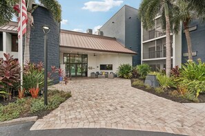 A hotel entrance with a paved driveway, a glass door, and a small seating area with chairs. - Landing Apartments Near HCA Florida Fawcett Hospital (Port Charlotte)
