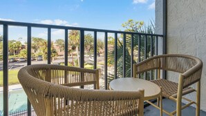 A balcony with wicker chairs and a small table, overlooking a parking lot and greenery. - Landing Apartments Near HCA Florida Fawcett Hospital (Port Charlotte)