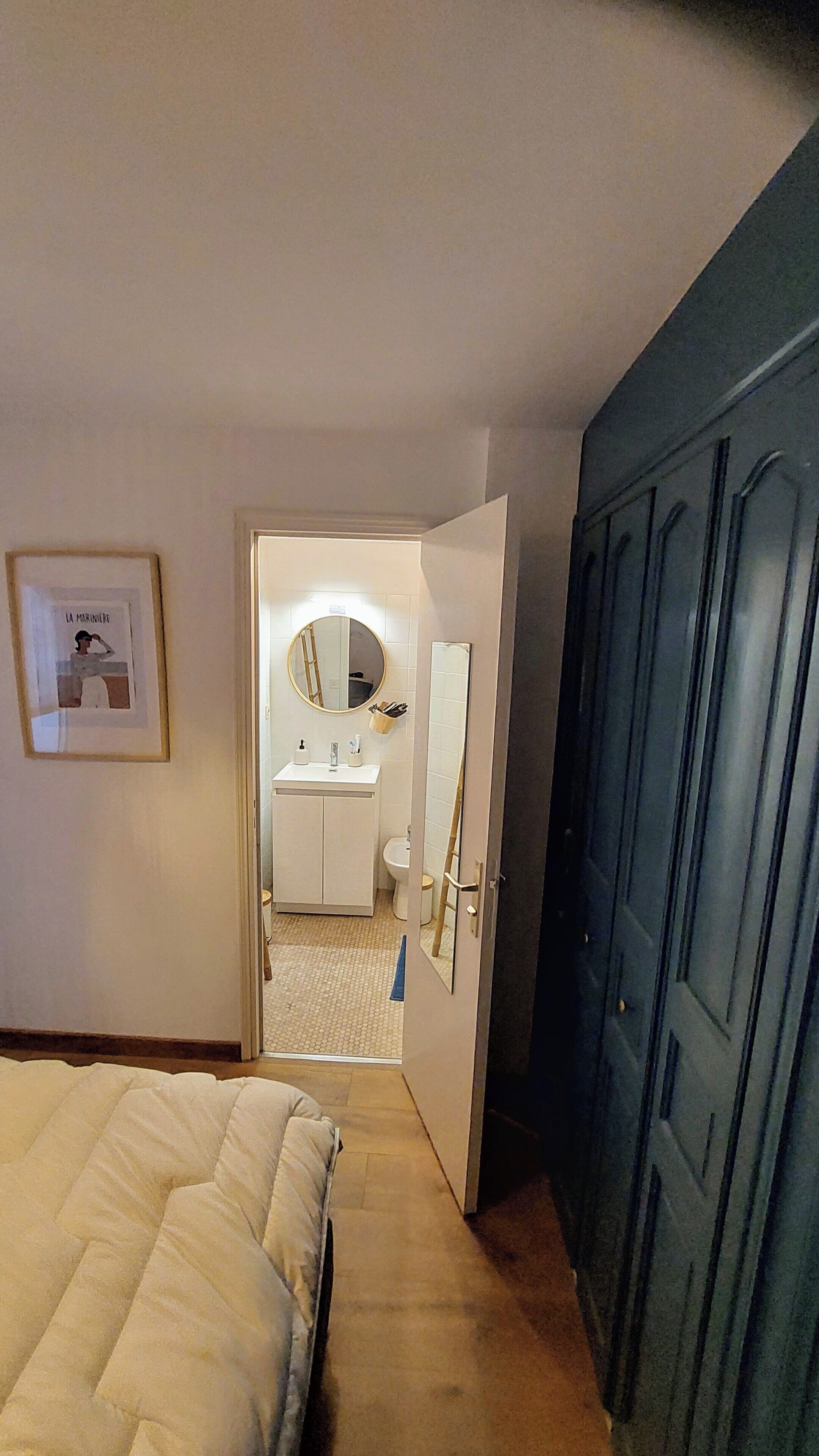 A bedroom with a bed, a door, and a bathroom visible through an open door.