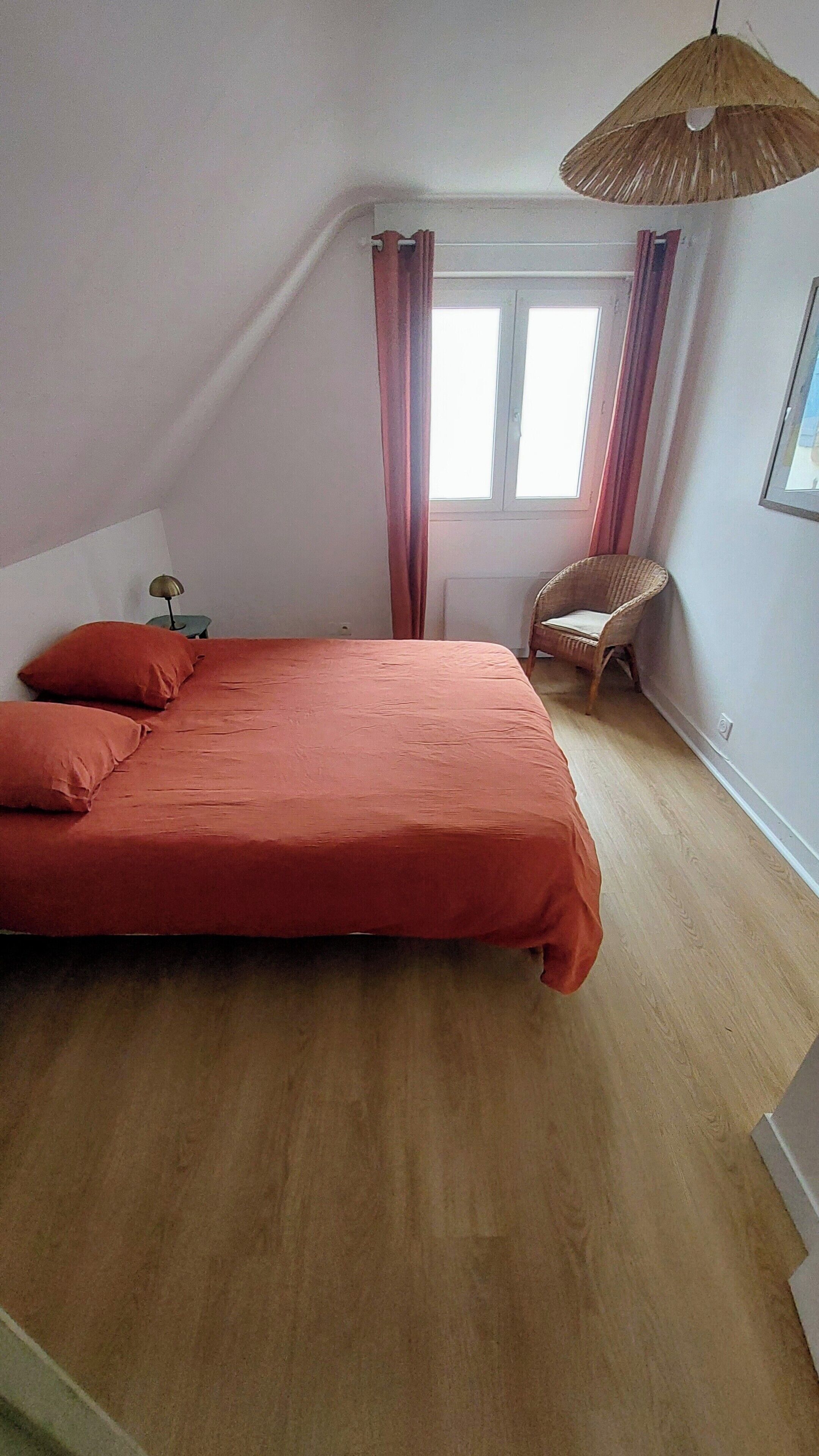 Ein Schlafzimmer mit Bett, Stuhl, Fenster und einer Pendelleuchte.