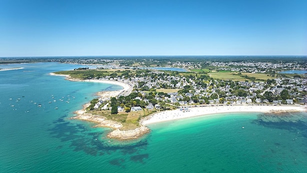 Ett flygbildsbild av en kuststad med en strand, klart turkosfärgat vatten och bostadsområden.