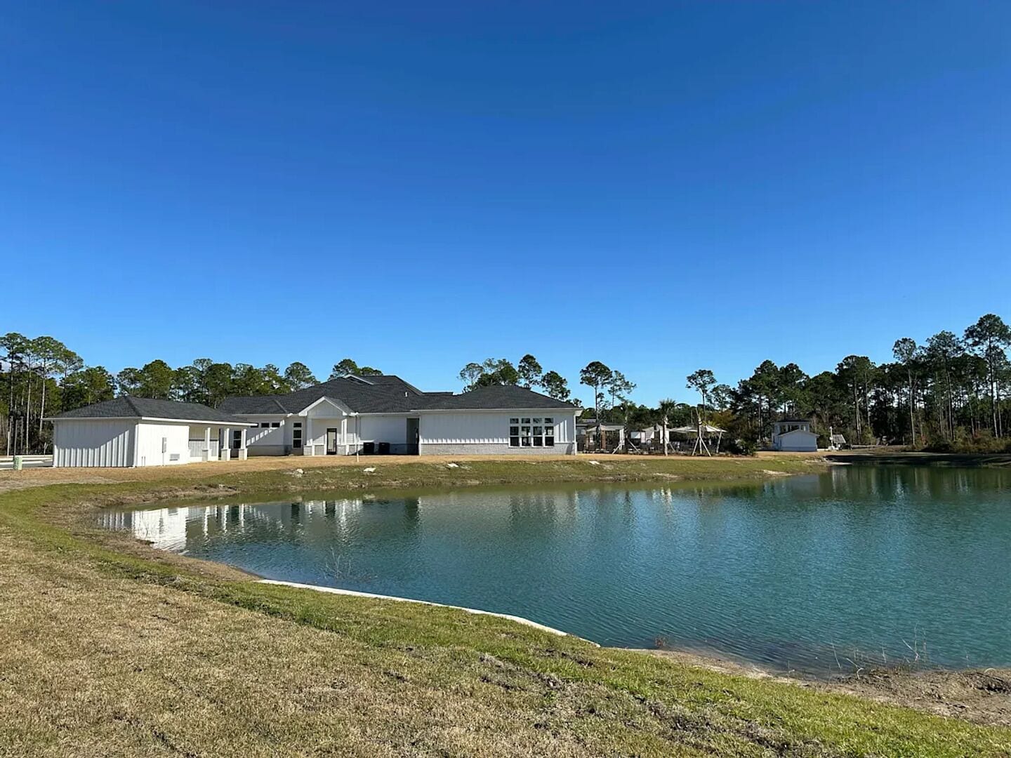 Um edifício grande com várias seções, um lago em primeiro plano e árvores ao fundo.