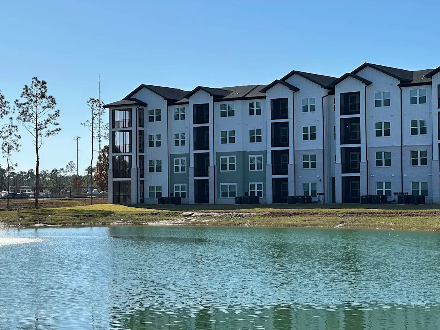 A multi-story residential building with a flat roof, large windows, and a grassy area in front.