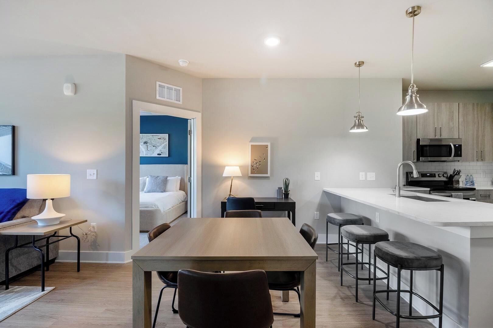 A modern hotel room with a dining area, kitchenette, and a separate bedroom.