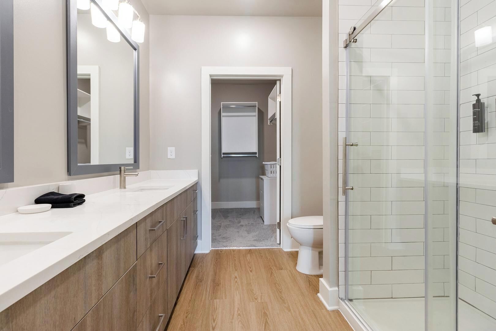 Een moderne badkamer met een grote spiegel, twee wastafels, een douchecabine en een toilet.