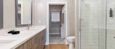 A modern bathroom with a large mirror, dual sinks, a shower enclosure, and a toilet.