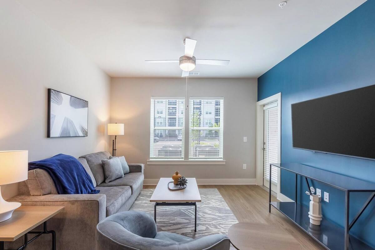 A modern living room with a sofa, coffee table, lamp, and a flat-screen TV mounted on a blue wall.