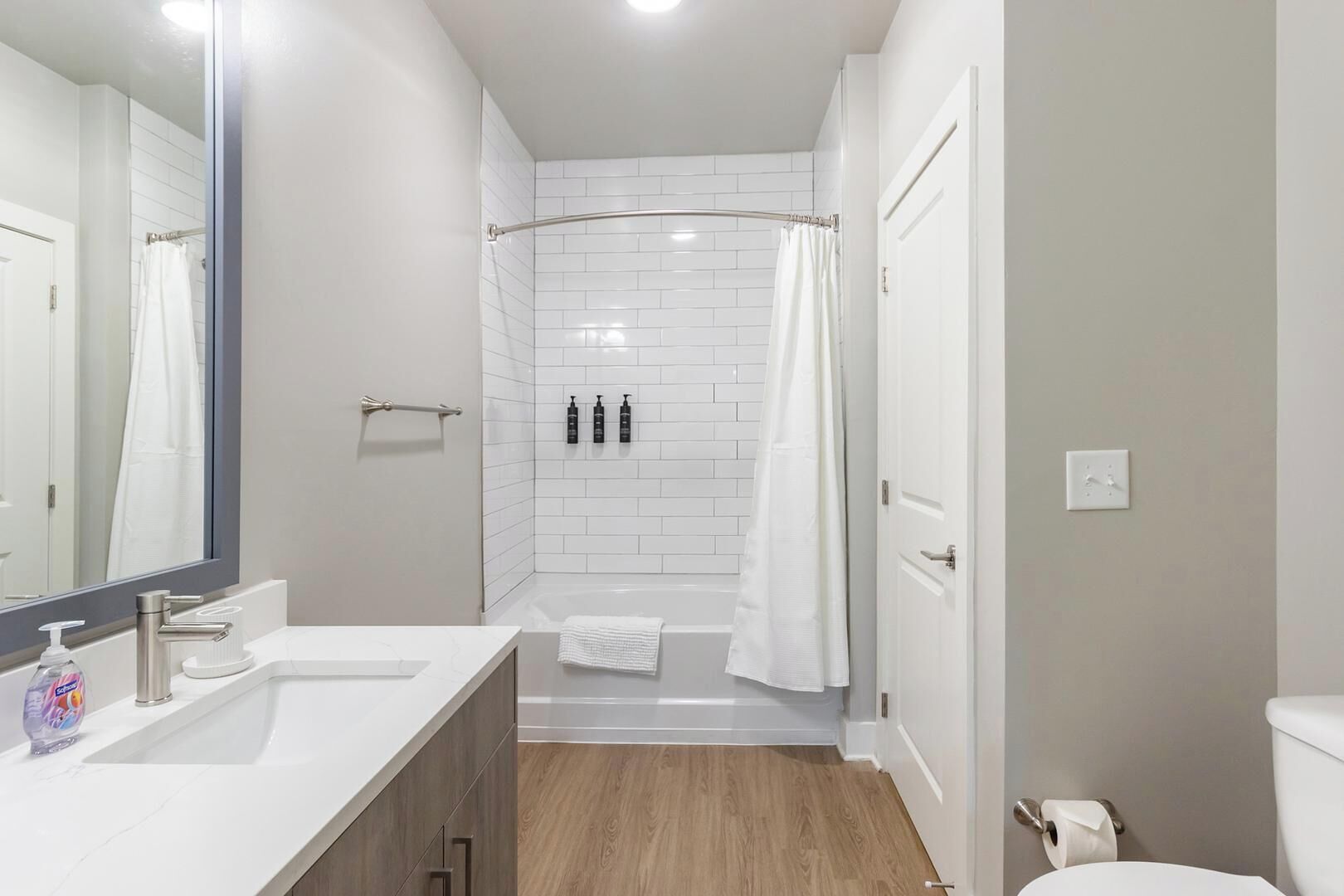 A modern bathroom with a white vanity, a large mirror, a shower with a glass door, and a toilet.