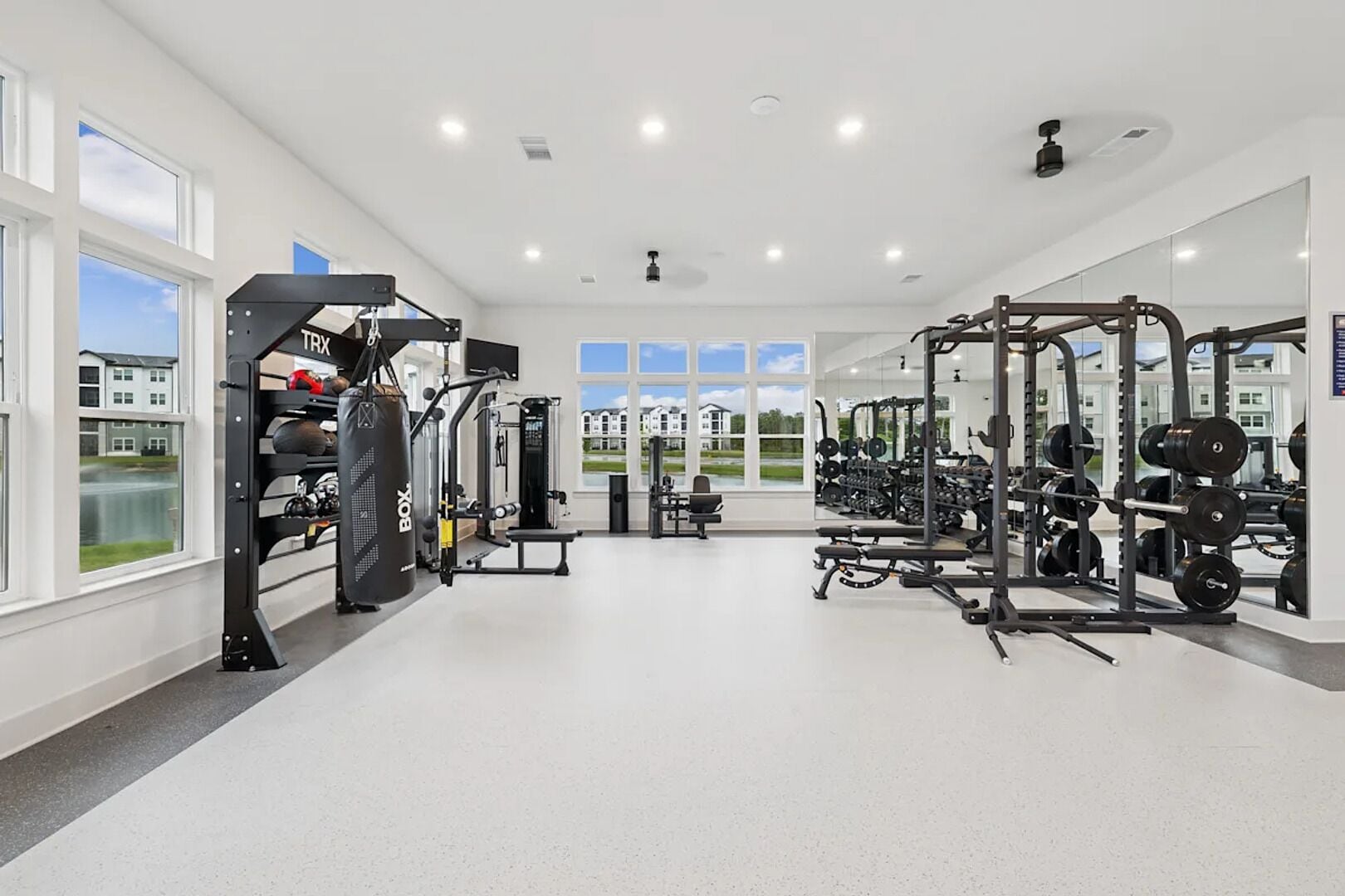 A spacious gym with various exercise equipment, large windows, and a view of the outside.