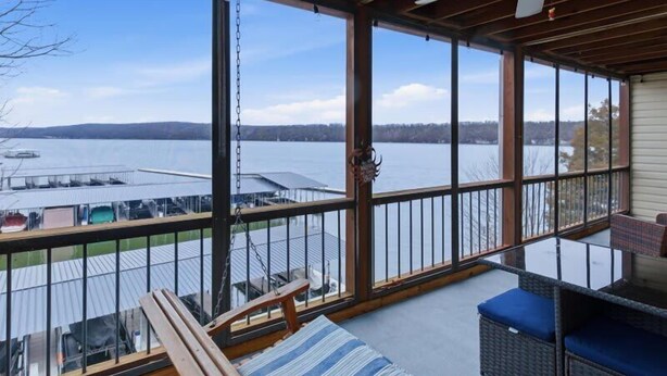 Um deck coberto ao ar livre com vista para um lago, móveis de madeira e um ventilador de teto.