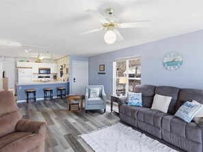 A living room with a grey sofa, a brown armchair, a white rug, a ceiling fan, and a kitchen area with a bar counter and stools. - |Lake Front | Views | Seasonal Pool | 3B 2B |Grill (Osage Beach)
