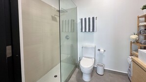 Une salle de bain avec une douche à parois de verre, des toilettes et une étagère avec des serviettes pliées.