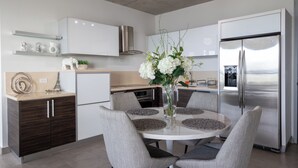Une cuisine moderne avec une table à manger, des chaises, un réfrigérateur, des placards et un vase rempli de fleurs.