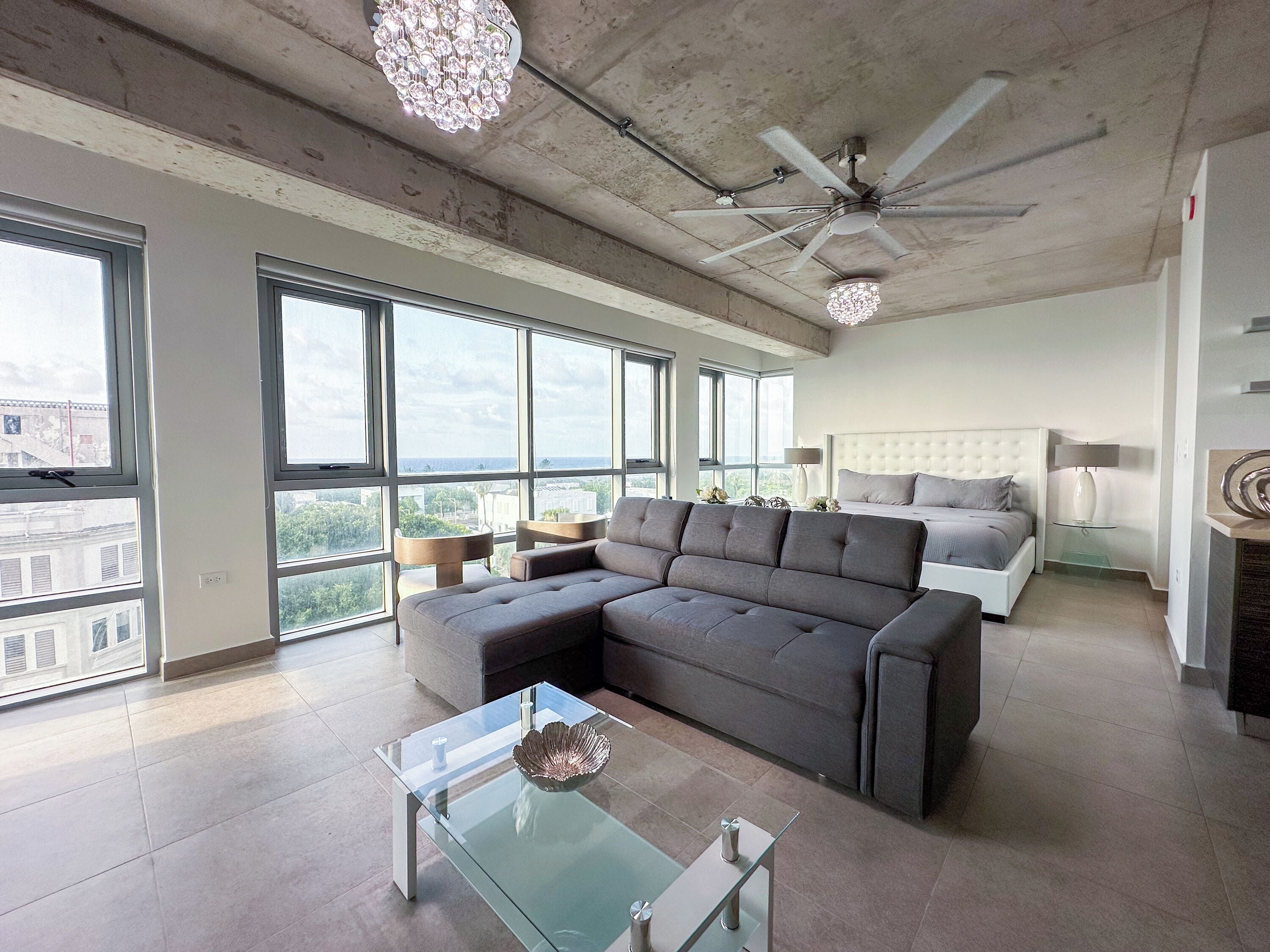 A modern living room with a sectional sofa, a glass coffee table, and a ceiling fan.