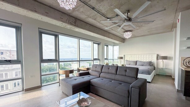 Un salon moderne avec un canapé d’angle, une table basse en verre et un ventilateur de plafond.