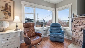 A room with a large window, a globe, a lamp, a brown leather chair, a blue leather chair, and a fireplace. - Historic PNW Bungalow - Sunset & Water View (Everett)