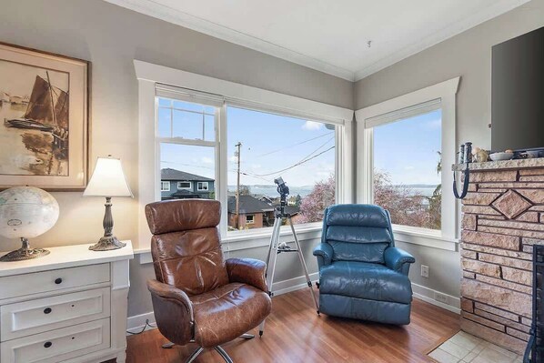 A room with a large window, a globe, a lamp, a brown leather chair, a blue leather chair, and a fireplace.