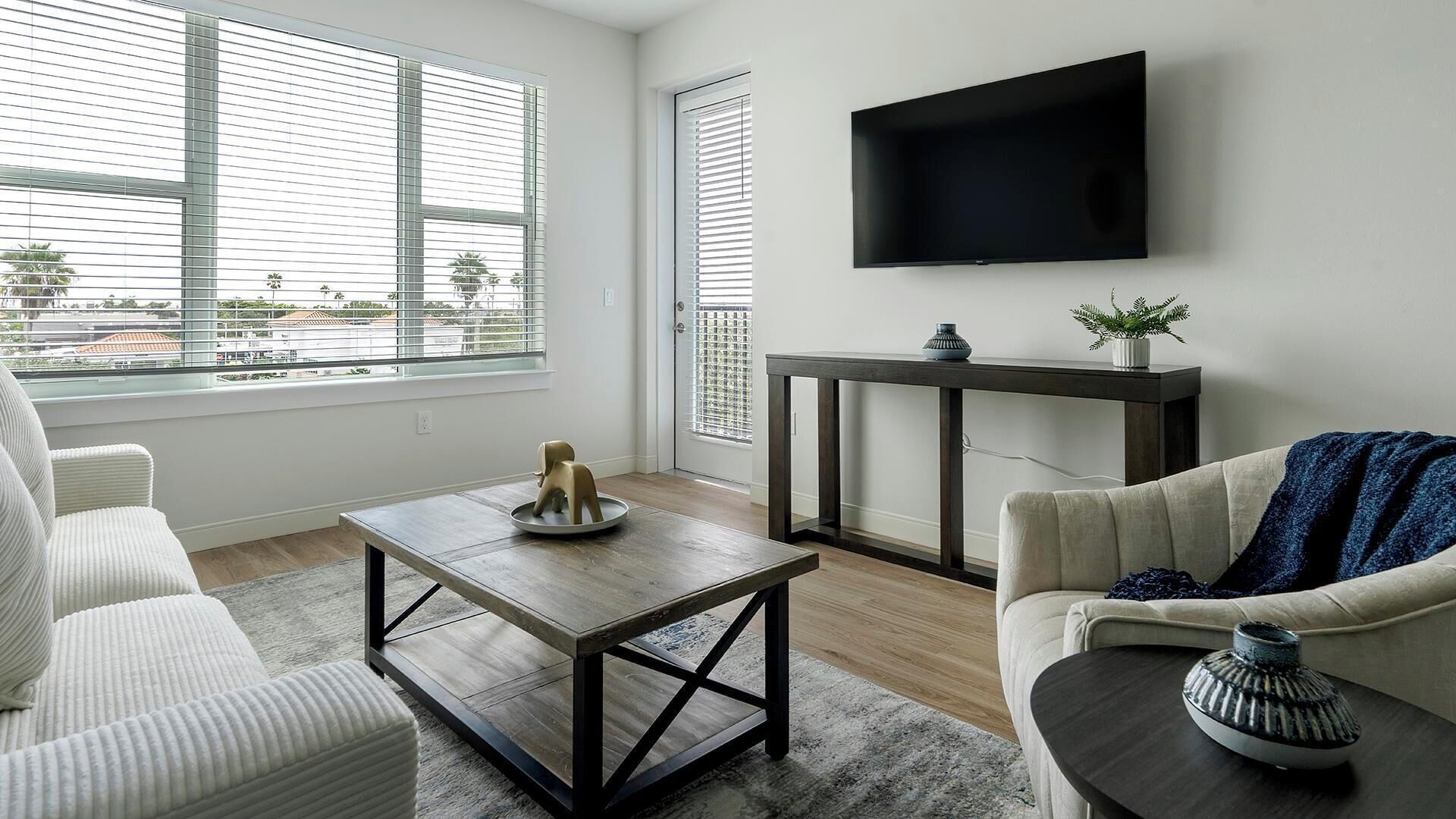 A modern living room with a large window, a flat-screen TV, a wooden coffee table, and a sofa.