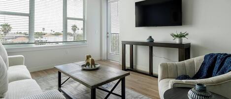 A modern living room with a large window, a flat-screen TV, a wooden coffee table, and a sofa.