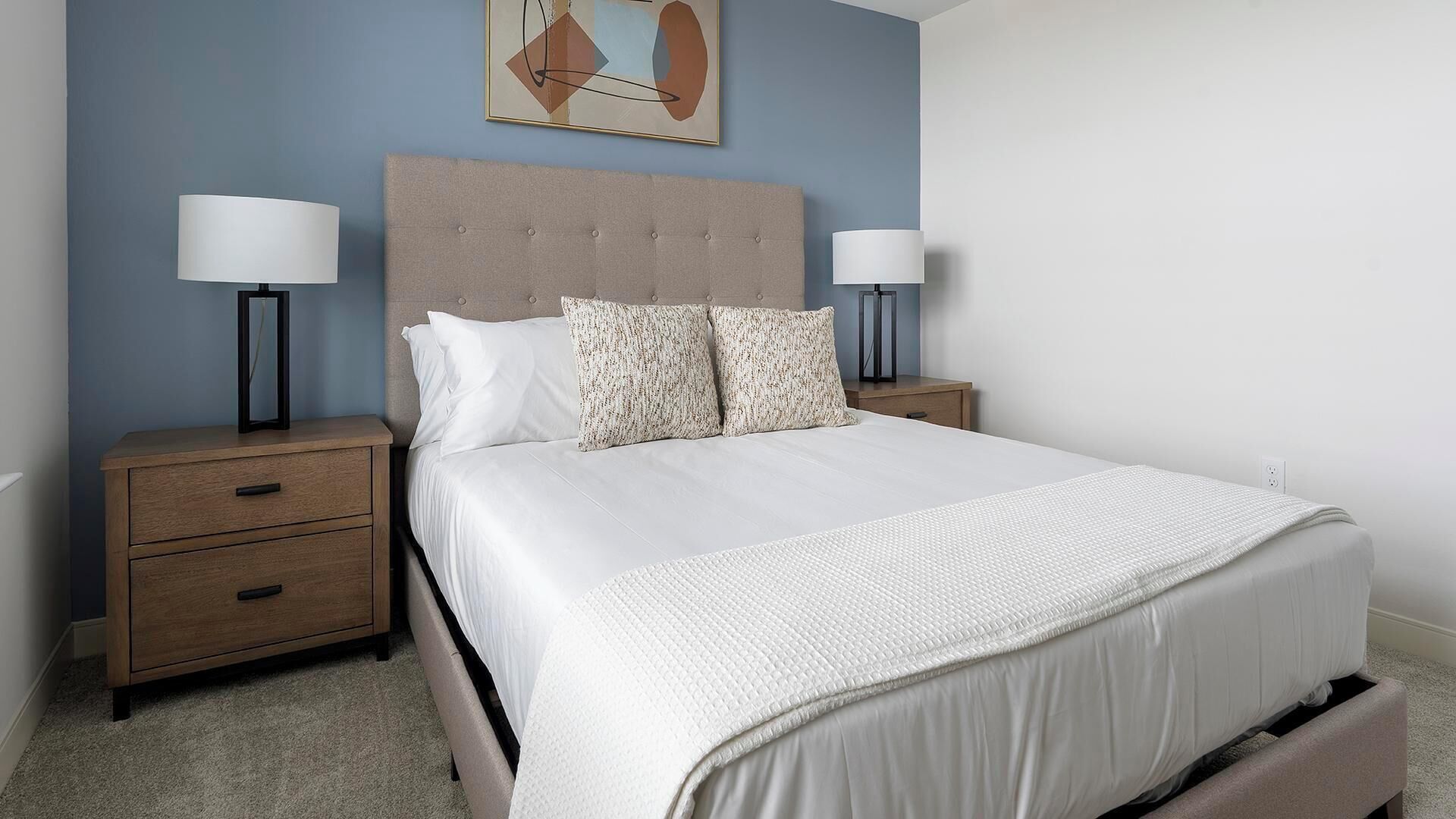 A bedroom with a bed, two bedside tables, a nightstand, a headboard, and a wall-mounted lamp.