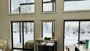 Een modern interieur met een bank, een eettafel en uitzicht op een besneeuwd landschap door grote ramen.