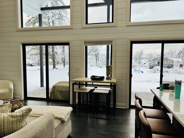 Ein modernes Interieur mit einer Couch, einem Esstisch und Blick auf eine verschneite Landschaft durch große Fenster.