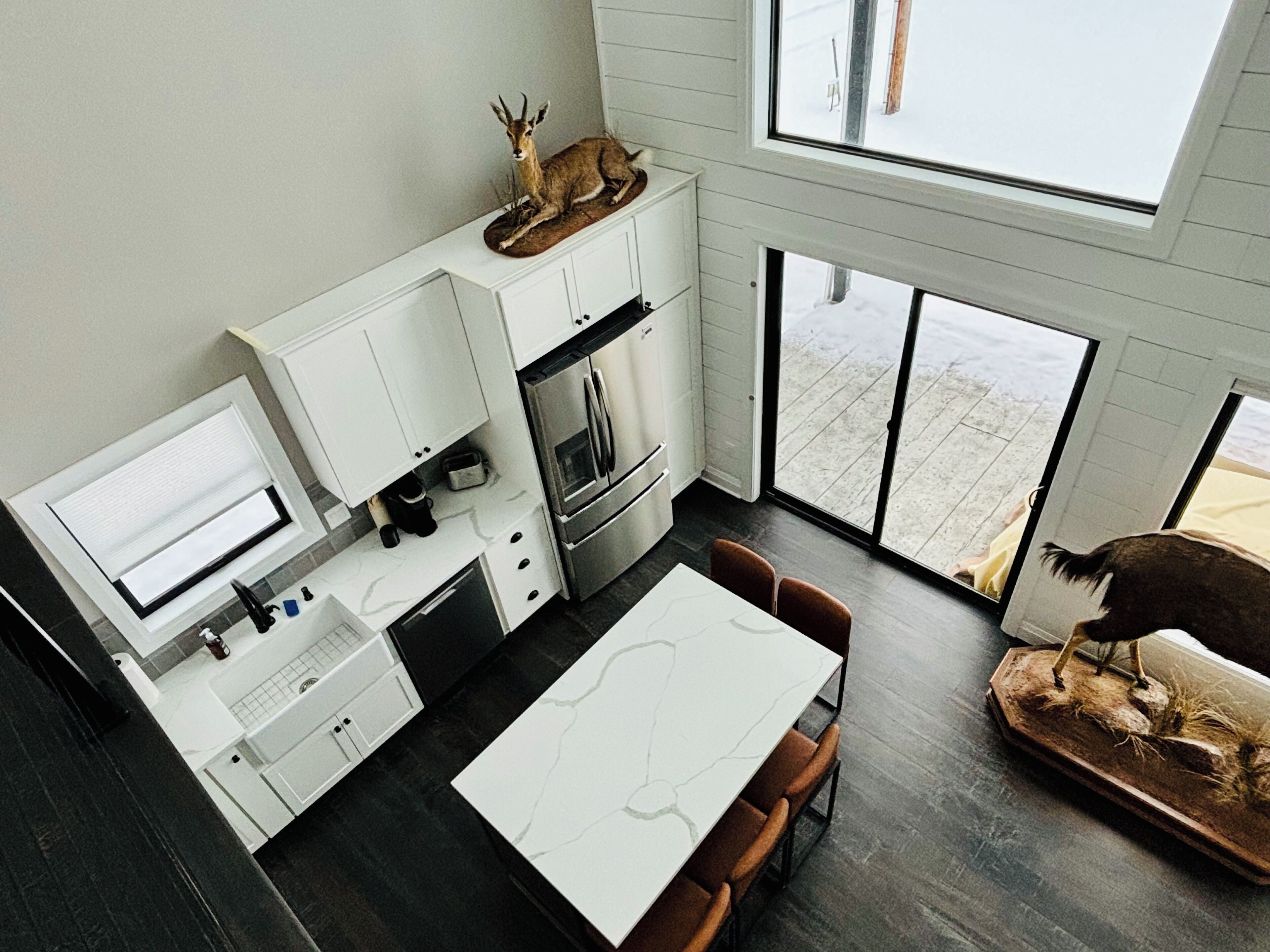 Una cocina moderna con armarios blancos, un comedor con mesa de mármol y un amplio ventanal.