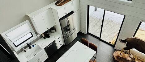 Una cocina moderna con armarios blancos, un comedor con mesa de mármol y un amplio ventanal.
