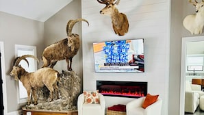 Een woonkamer met een open haard, bevestigde hertenhoorns en een televisie waarop een advertentie wordt getoond.