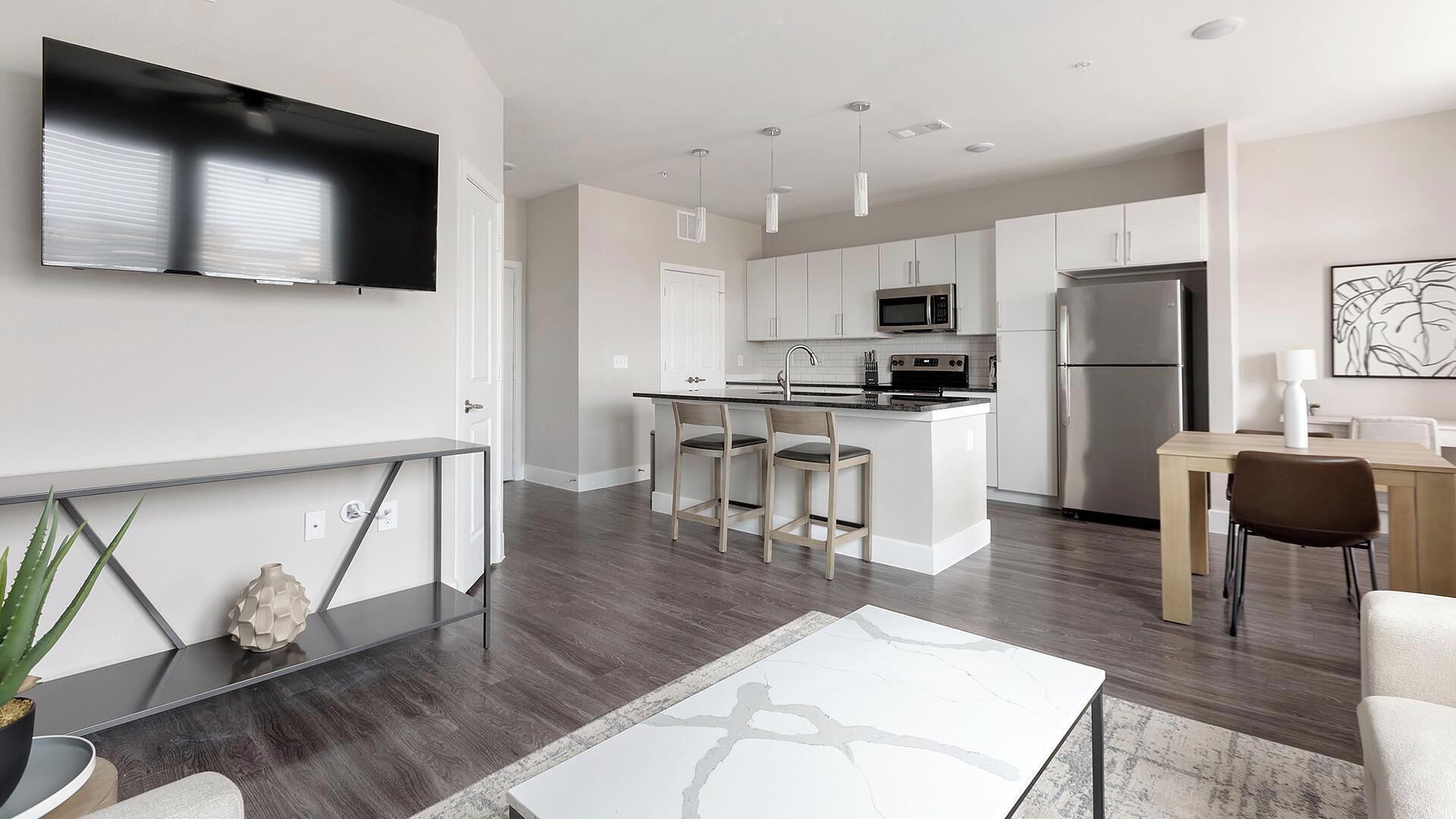 A modern kitchen with a central island, white cabinetry, stainless steel appliances, and a flat-screen TV mounted on the wall.