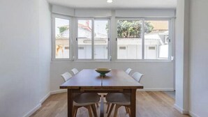 A dining area with a table and chairs, large windows, and a view of buildings outside. - Village Carcavelos II - Refuge with private backyard 7 minutes from the beach (Carcavelos)