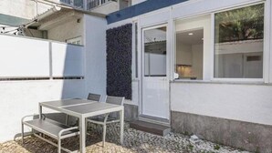 A patio with a metal table and chairs, a door leading to an interior space, and a wall with a textured pattern. - Village Carcavelos II - Refuge with private backyard 7 minutes from the beach (Carcavelos)