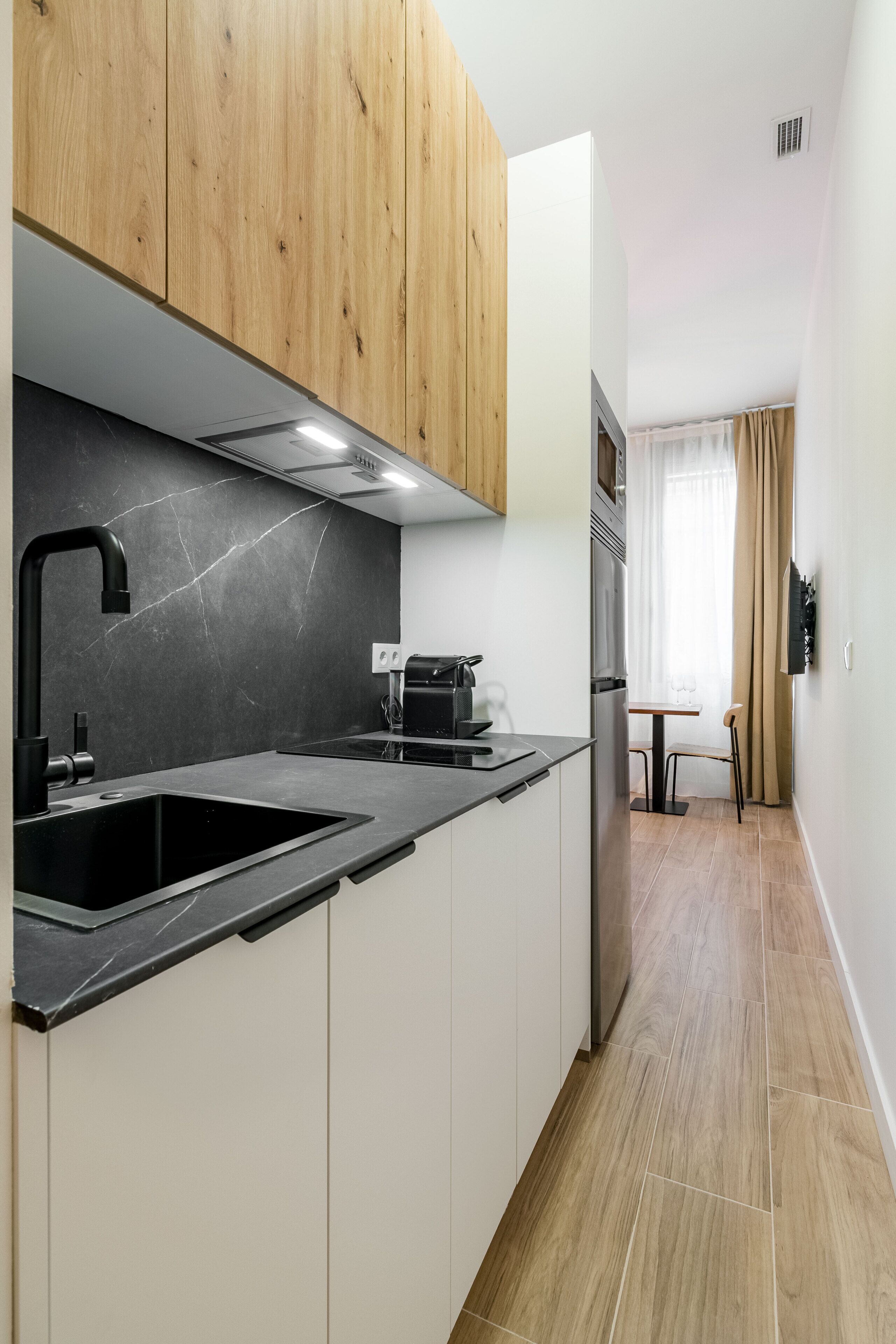 A modern kitchen with wooden cabinets, a black countertop, and a stainless steel refrigerator.