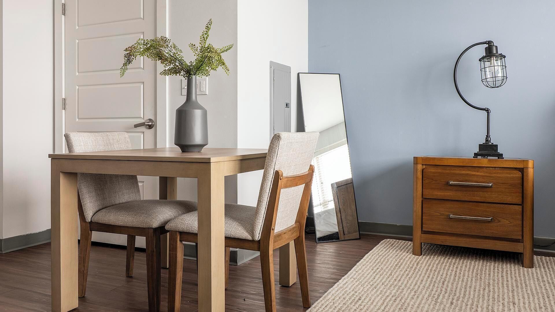 Ein Essbereich mit einem Holztisch, zwei Stühlen, einer Pflanzvase, einer Lampe und einem Schrank.