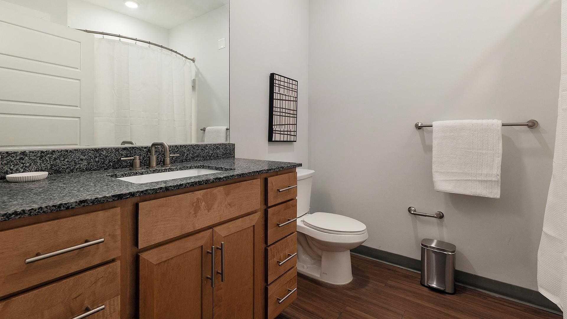 A modern bathroom with a granite countertop, wooden cabinets, a white toilet, and a towel rack.