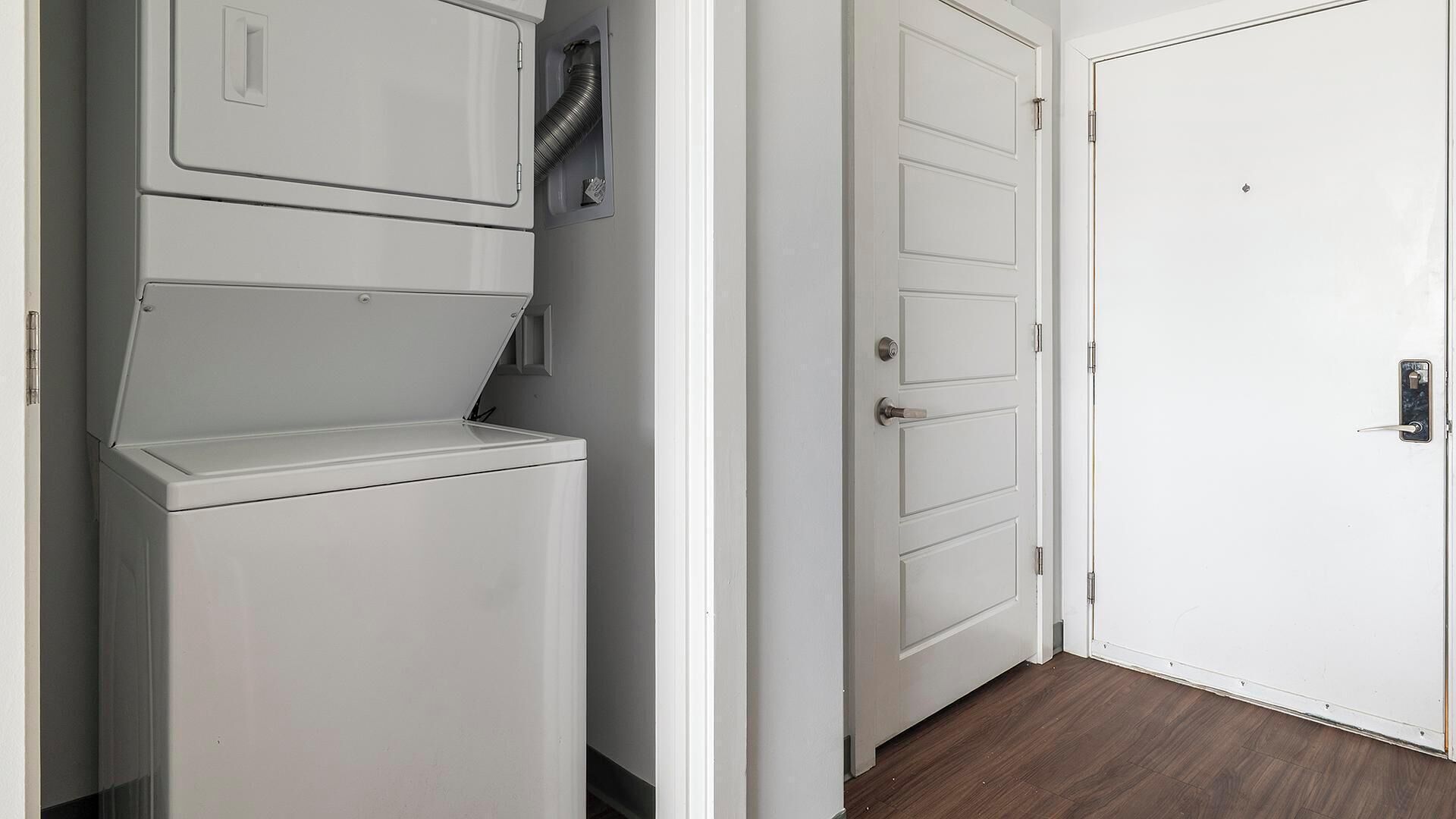 A laundry room with a white washing machine and dryer, a vent, and a white door with a handle.