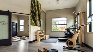Un gimnasio con equipo de ejercicio, una planta en la pared y una ventana que proporciona luz natural.