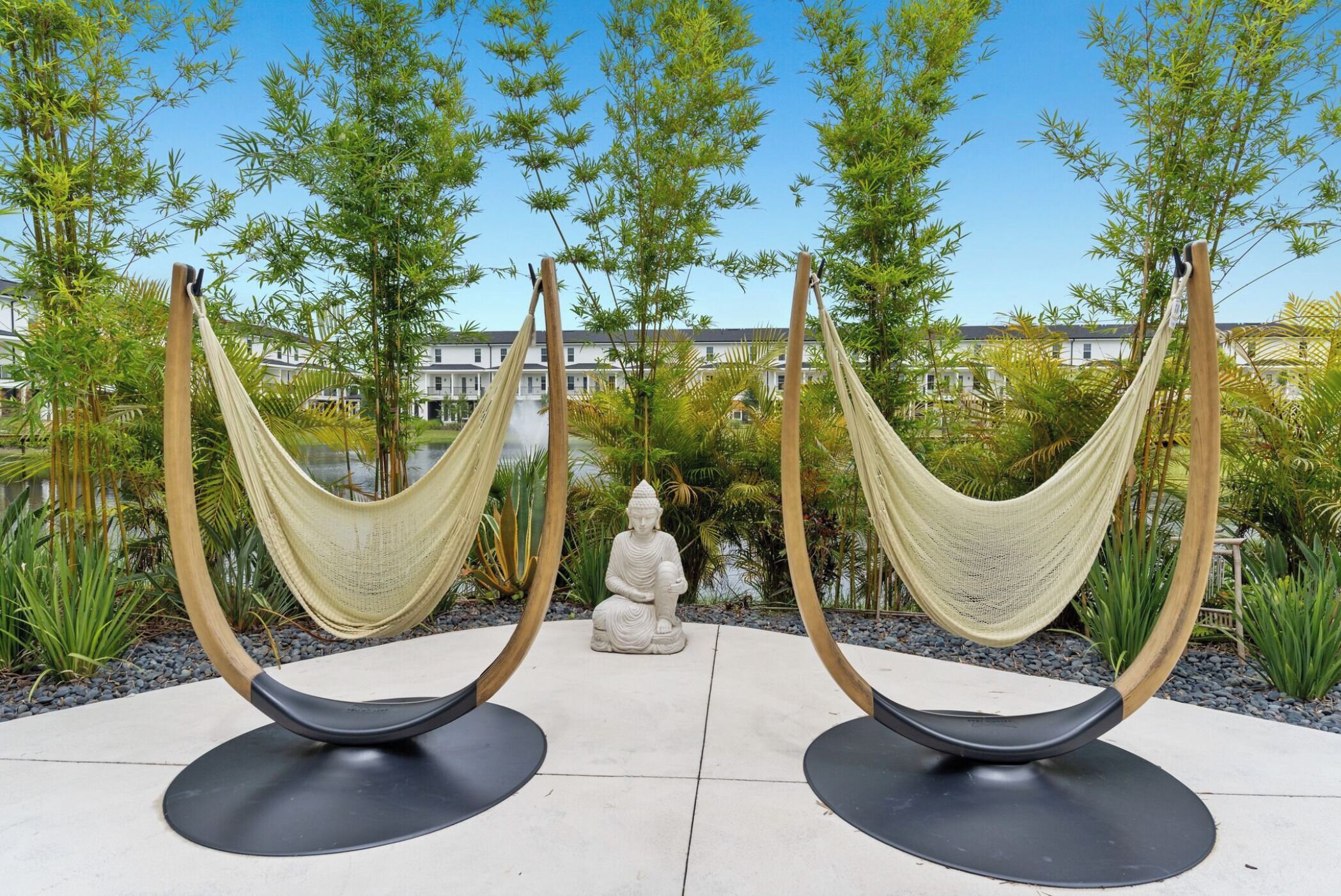 A serene outdoor area with two hammocks, a Buddha statue, and lush greenery.