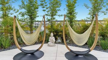 A serene outdoor area with two hammocks, a Buddha statue, and lush greenery.