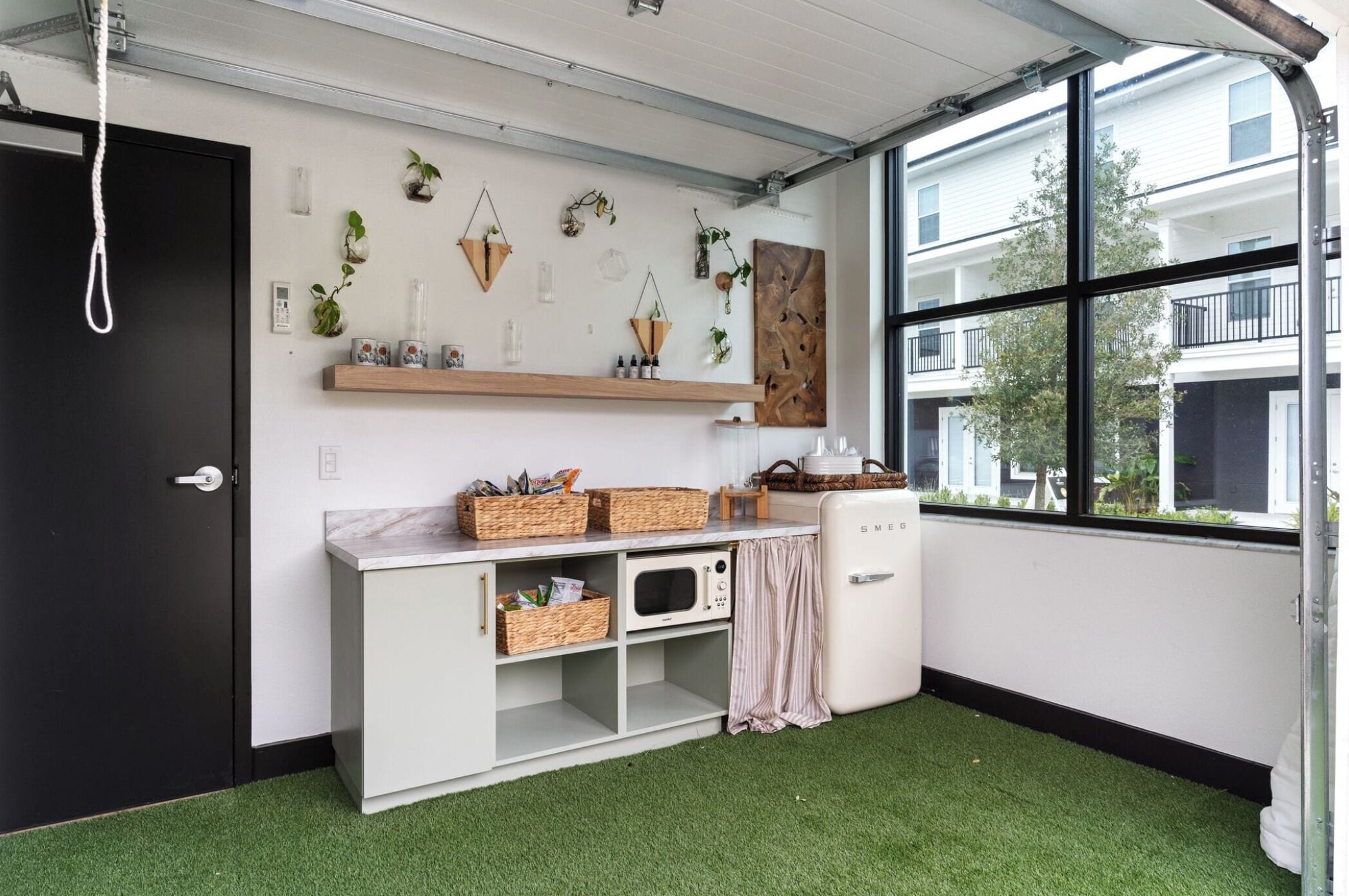 Een compacte keuken met een magnetron, een kleine koelkast en een plank met planten en keukengerei.