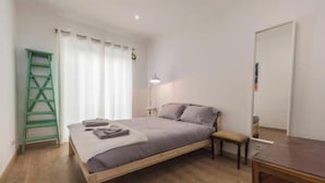 Een slaapkamer met een houten bed, een groene ladder, een nachtkastje en een spiegel.