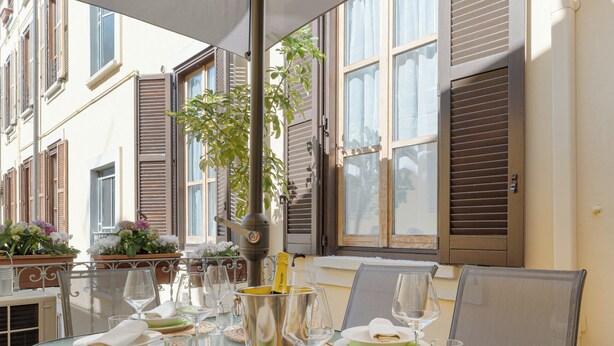 Un área de comedor al aire libre con una mesa dispuesta para cuatro personas, rodeada de sillas y cubierta por una pérgola.