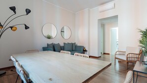 Una habitación amplia con una gran mesa de madera, un sofá, dos espejos redondos y una lámpara fijada a la pared.