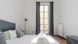 Una habitación de hotel con una cama, un radiador, un sofá gris y una ventana con cortinas.